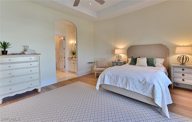 bedroom with wood finished floors, baseboards, arched walkways, ceiling fan, and ensuite bathroom