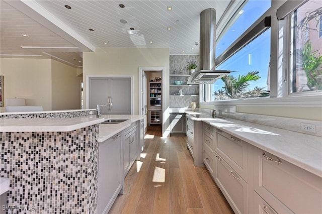 kitchen featuring light wood finished floors, a sink, light stone counters, island exhaust hood, and open shelves