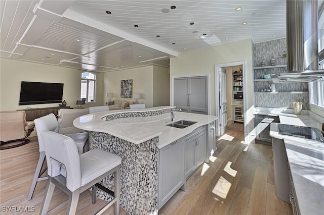 kitchen with an island with sink, a sink, light stone counters, wood finished floors, and exhaust hood