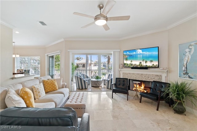 living room with crown molding, a wealth of natural light, a tile fireplace, and ceiling fan