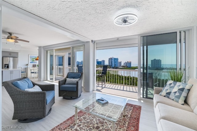 living room with a view of city, floor to ceiling windows, light wood-style flooring, ceiling fan, and a textured ceiling