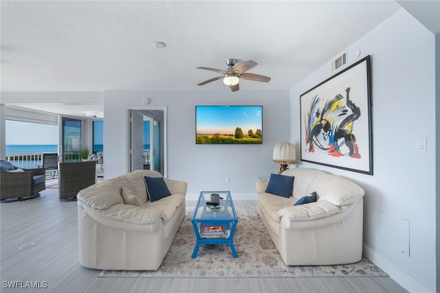 living area featuring light wood finished floors, a water view, visible vents, ceiling fan, and baseboards