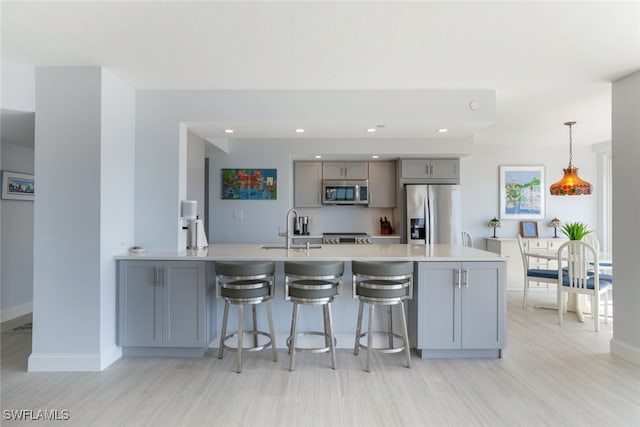 kitchen with hanging light fixtures, gray cabinets, stainless steel appliances, light countertops, and a sink