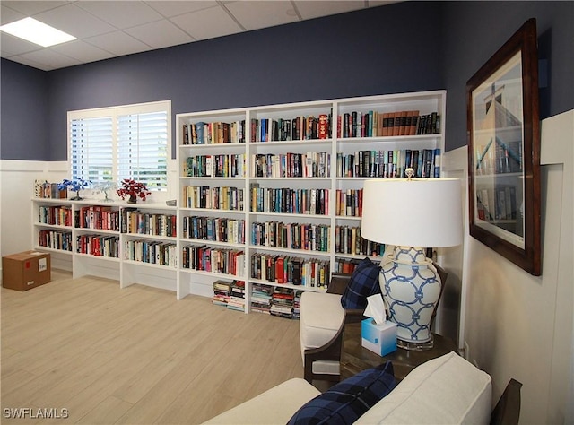 sitting room with bookshelves, wood finished floors, and a paneled ceiling