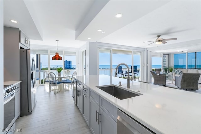 kitchen featuring hanging light fixtures, a water view, stainless steel appliances, light countertops, and a sink