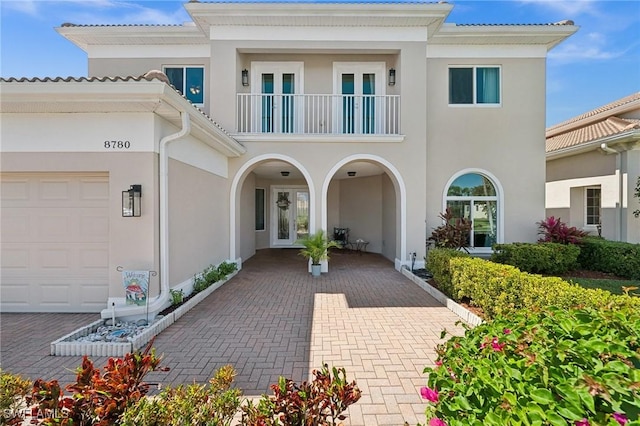 exterior space with stucco siding, french doors, an attached garage, and a balcony