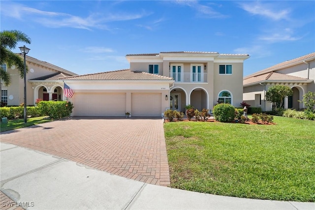 mediterranean / spanish-style home with stucco siding, decorative driveway, an attached garage, a front yard, and a balcony