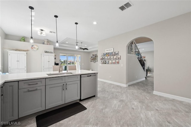 kitchen featuring baseboards, a tray ceiling, gray cabinets, stainless steel dishwasher, and a sink