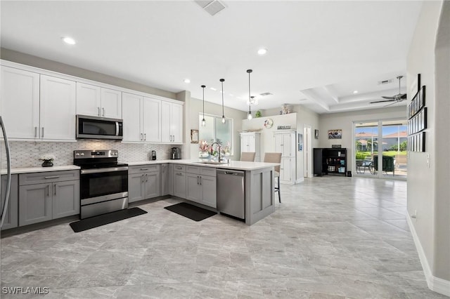 kitchen with open floor plan, decorative backsplash, gray cabinets, stainless steel appliances, and a sink