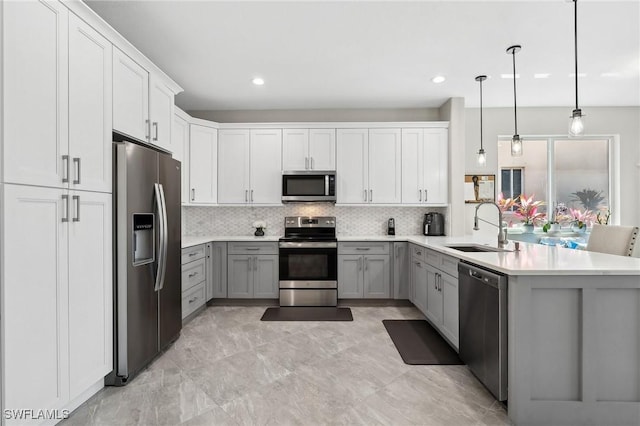 kitchen with backsplash, gray cabinetry, appliances with stainless steel finishes, a peninsula, and a sink