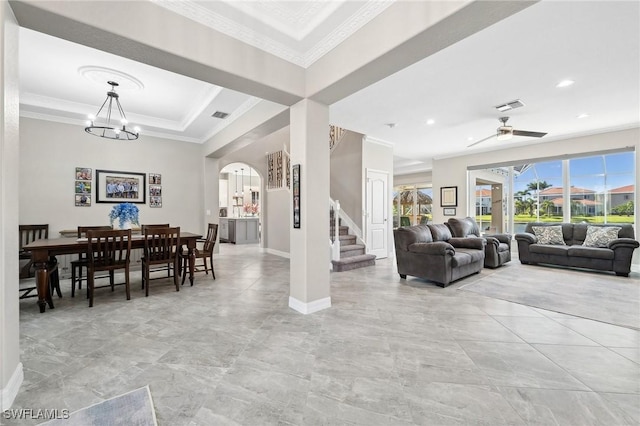 living room featuring visible vents, crown molding, stairs, ceiling fan with notable chandelier, and arched walkways