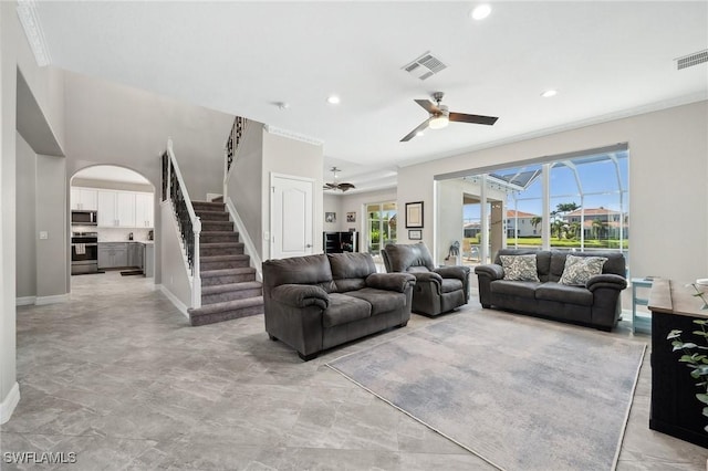 living area featuring stairs, visible vents, arched walkways, and a ceiling fan