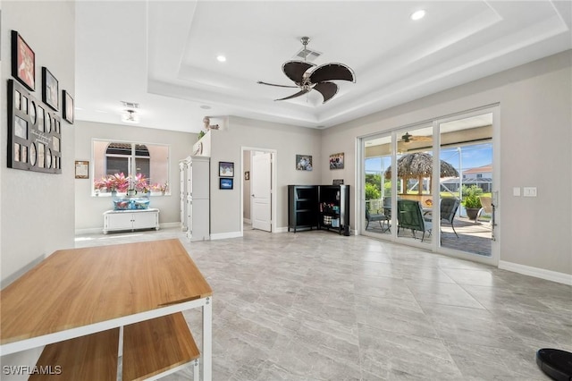 unfurnished living room featuring a tray ceiling, baseboards, visible vents, and ceiling fan