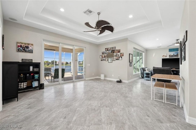 living room with a raised ceiling, a ceiling fan, visible vents, and baseboards