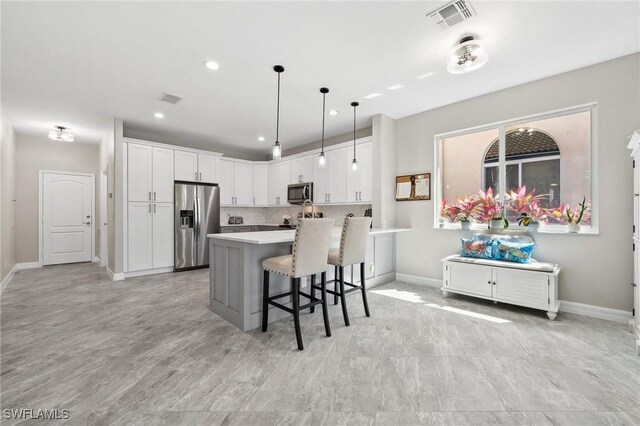 kitchen with visible vents, light countertops, a kitchen breakfast bar, stainless steel appliances, and white cabinetry