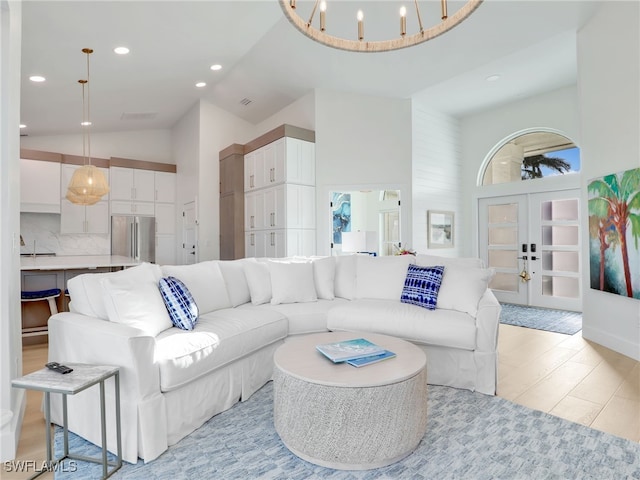 living room featuring light wood finished floors, high vaulted ceiling, recessed lighting, french doors, and a notable chandelier