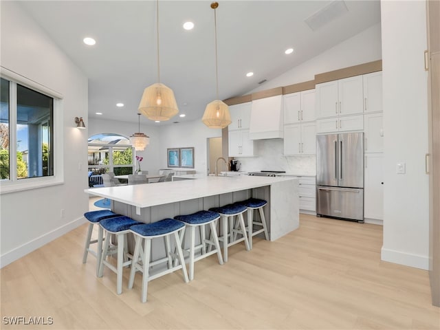 kitchen with a sink, tasteful backsplash, freestanding refrigerator, white cabinets, and custom exhaust hood