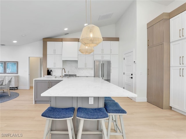 kitchen with white cabinetry, high quality fridge, an island with sink, and vaulted ceiling