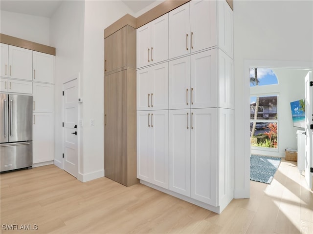 kitchen with baseboards, a high ceiling, white cabinetry, high quality fridge, and light wood-type flooring