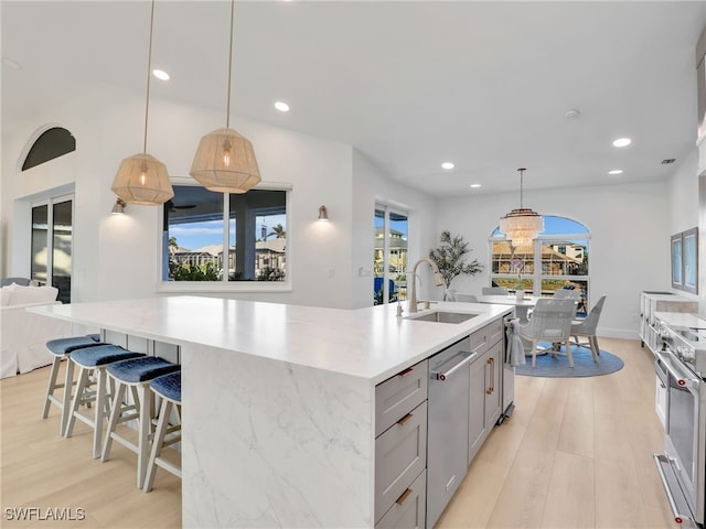 kitchen featuring light wood-type flooring, gray cabinetry, a kitchen island with sink, a sink, and appliances with stainless steel finishes