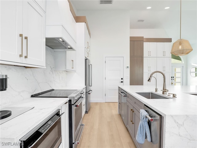 kitchen with a sink, light stone countertops, high quality appliances, and white cabinets