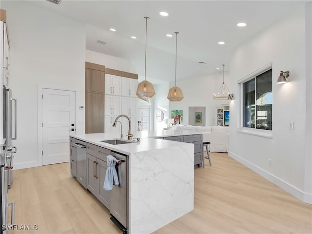 kitchen featuring pendant lighting, light wood-style floors, a large island with sink, and a sink