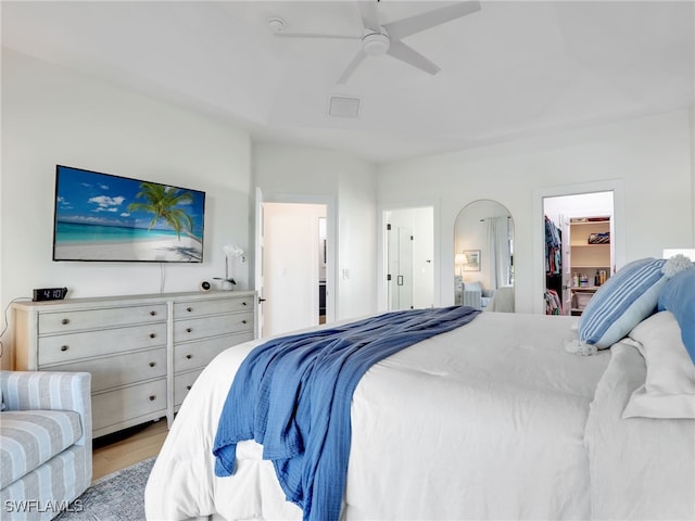 bedroom featuring visible vents, a walk in closet, a ceiling fan, wood finished floors, and arched walkways