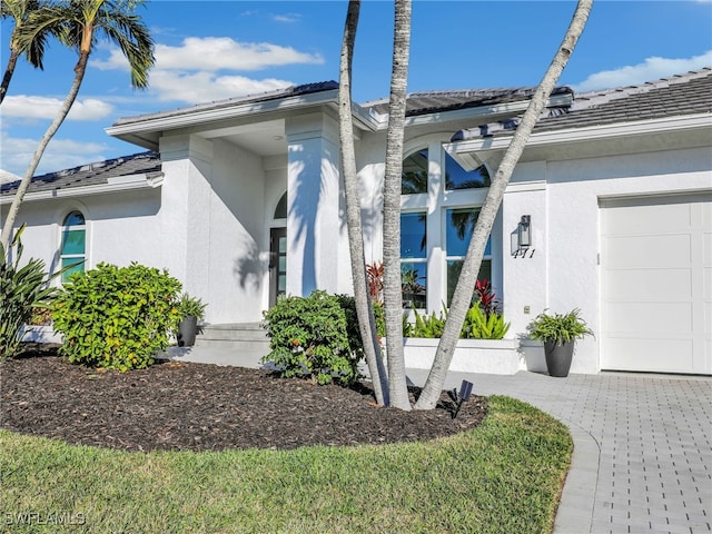 view of front of house featuring decorative driveway, an attached garage, and stucco siding