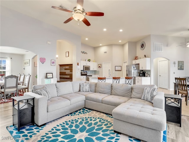 living room featuring sink, light hardwood / wood-style flooring, ceiling fan, and a high ceiling