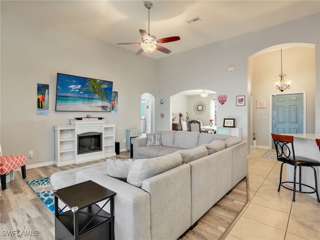 living room with a towering ceiling, light hardwood / wood-style floors, and ceiling fan with notable chandelier