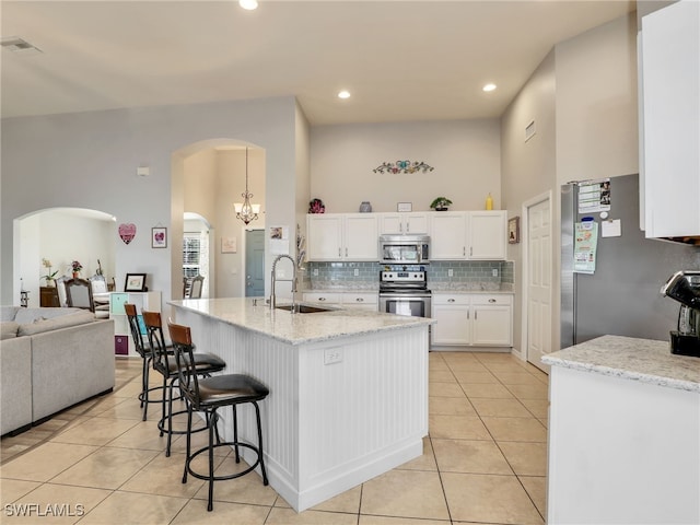 kitchen with sink, light tile patterned floors, appliances with stainless steel finishes, white cabinetry, and light stone counters