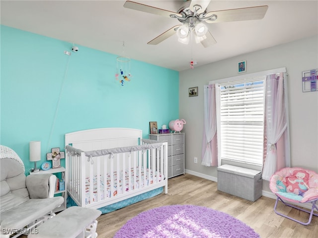 bedroom with a nursery area, ceiling fan, and light wood-type flooring