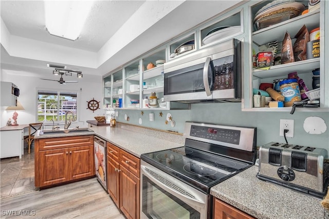 kitchen with light countertops, appliances with stainless steel finishes, brown cabinetry, a sink, and a peninsula