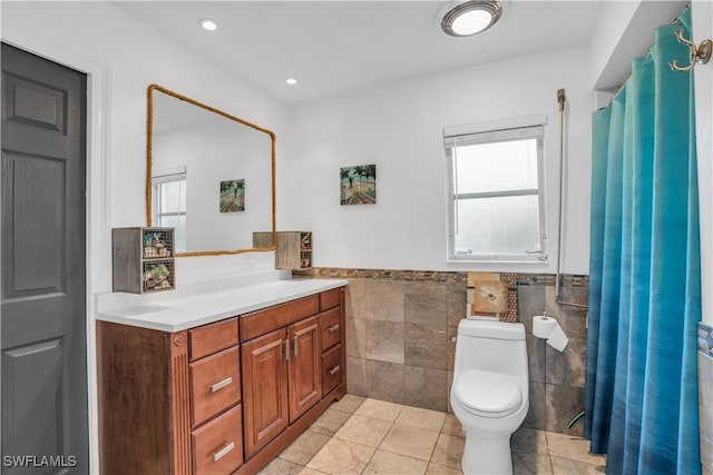 bathroom featuring a wainscoted wall, tile walls, recessed lighting, toilet, and vanity