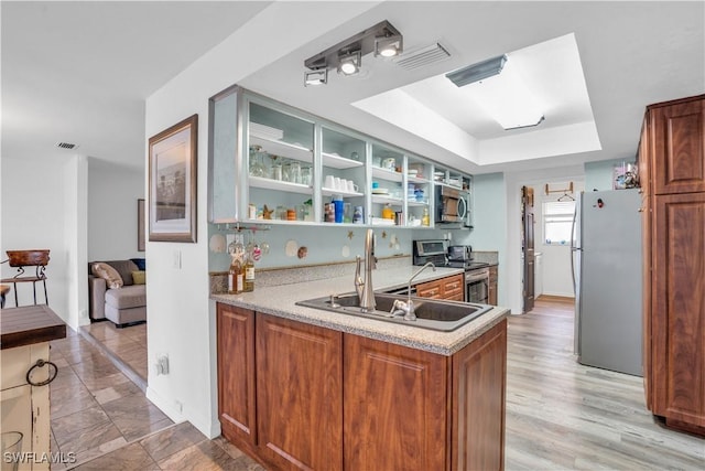 kitchen featuring stainless steel appliances, a raised ceiling, light countertops, a sink, and a peninsula