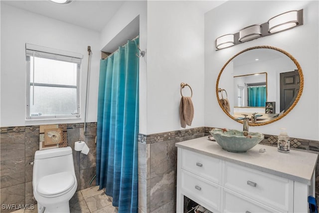 full bath with toilet, a wainscoted wall, vanity, and tile walls