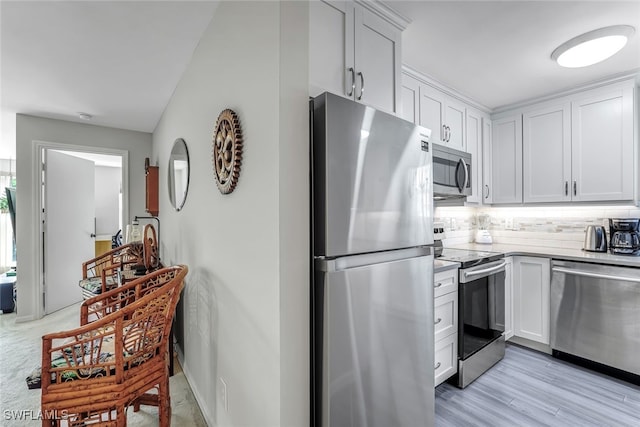 kitchen with appliances with stainless steel finishes, white cabinetry, light wood-style flooring, and backsplash