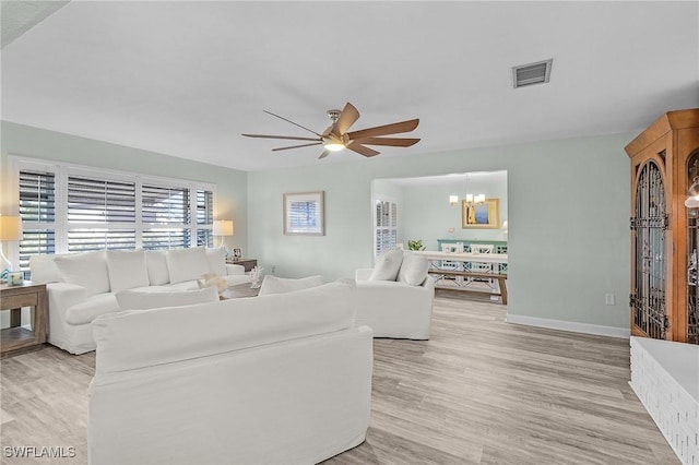 living room with ceiling fan with notable chandelier and light hardwood / wood-style flooring