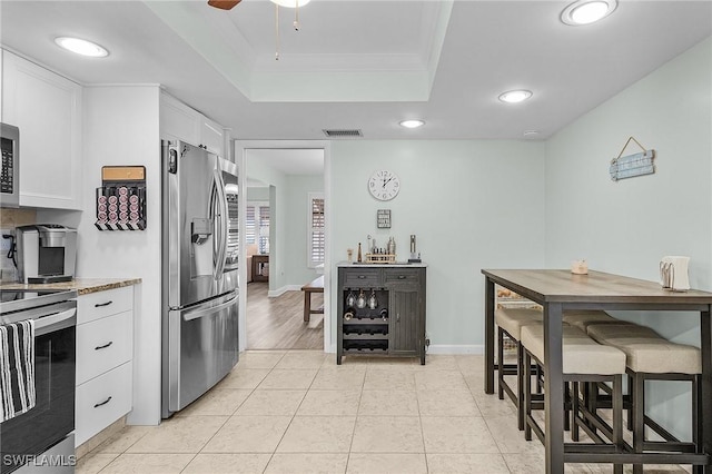 kitchen with light tile patterned flooring, white cabinetry, crown molding, a tray ceiling, and stainless steel appliances