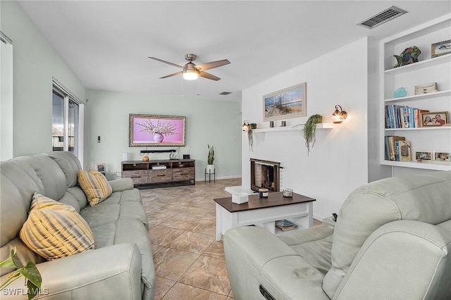 living room with a fireplace, built in features, and ceiling fan