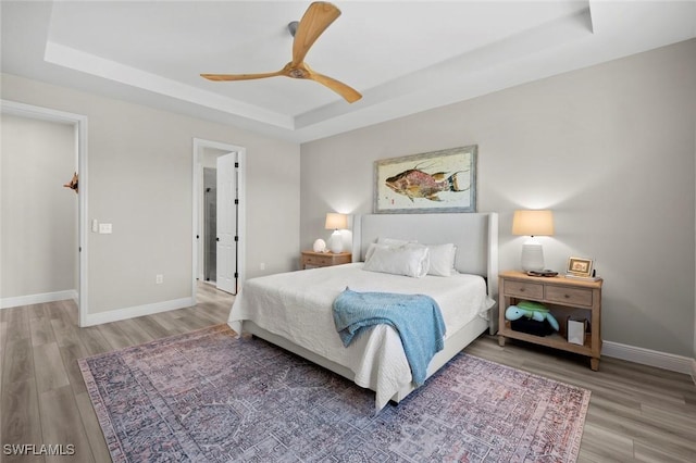 bedroom with a raised ceiling, ceiling fan, and wood-type flooring