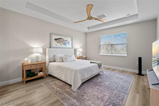 bedroom with a tray ceiling, light wood-type flooring, and ceiling fan