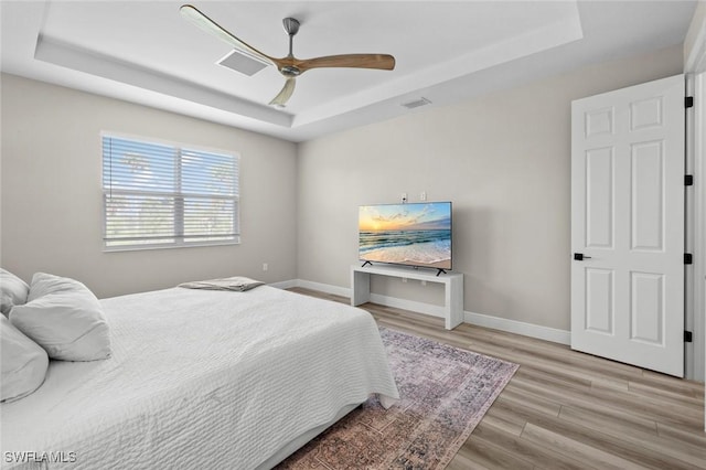 bedroom featuring ceiling fan, light wood-type flooring, and a raised ceiling