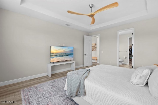 bedroom featuring a tray ceiling, hardwood / wood-style flooring, connected bathroom, and ceiling fan