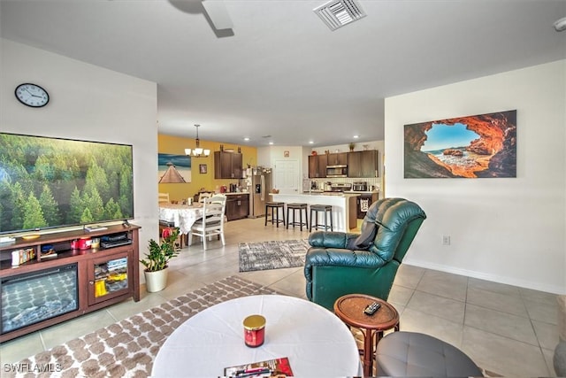 living area featuring light tile patterned floors, recessed lighting, ceiling fan with notable chandelier, visible vents, and baseboards