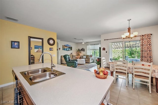 kitchen with a sink, visible vents, light countertops, hanging light fixtures, and a center island with sink