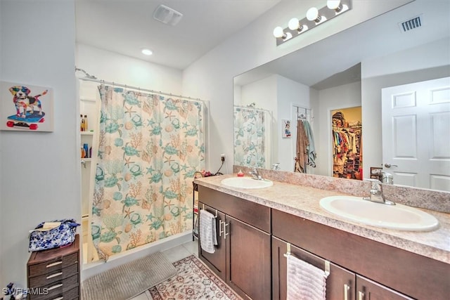 full bath with double vanity, a sink, a spacious closet, and tile patterned floors