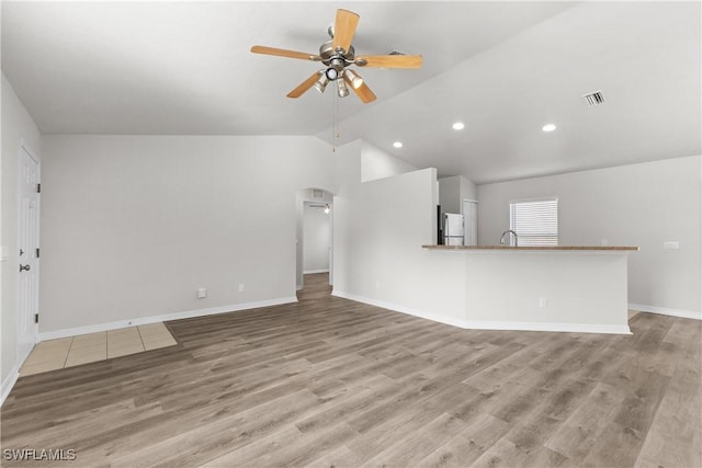 unfurnished living room with ceiling fan, light wood-type flooring, lofted ceiling, and baseboards