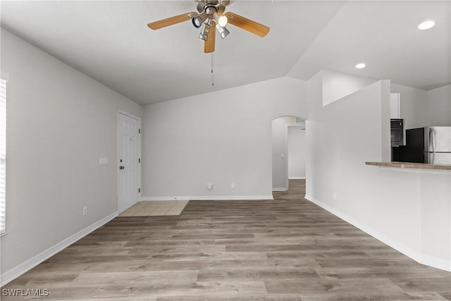 unfurnished living room featuring arched walkways, ceiling fan, vaulted ceiling, wood finished floors, and baseboards