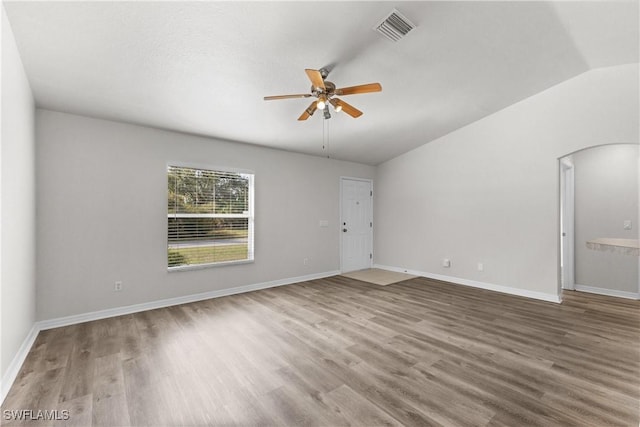 unfurnished room with arched walkways, vaulted ceiling, wood finished floors, and visible vents